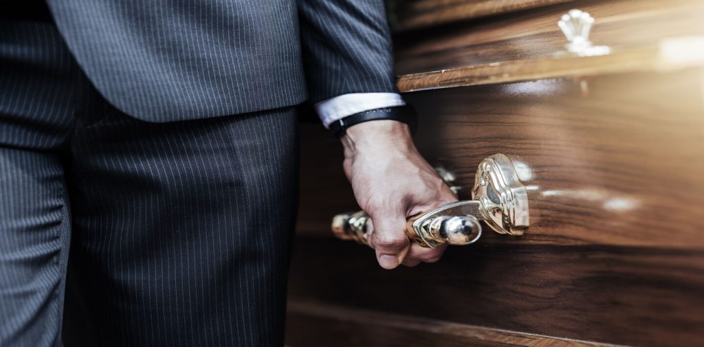 Poignée dorée de cercueil tenue par un porteur en costume - Organisation d'obsèques Claudepierre